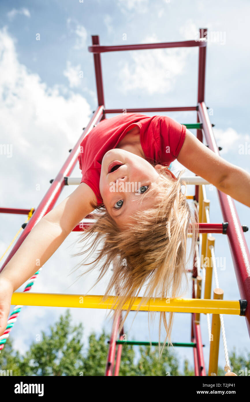 Elementary age girl hanging from a jungle gym (monkey bars or climbing frame) while playing in a playground - child safety or risky play concept Stock Photo