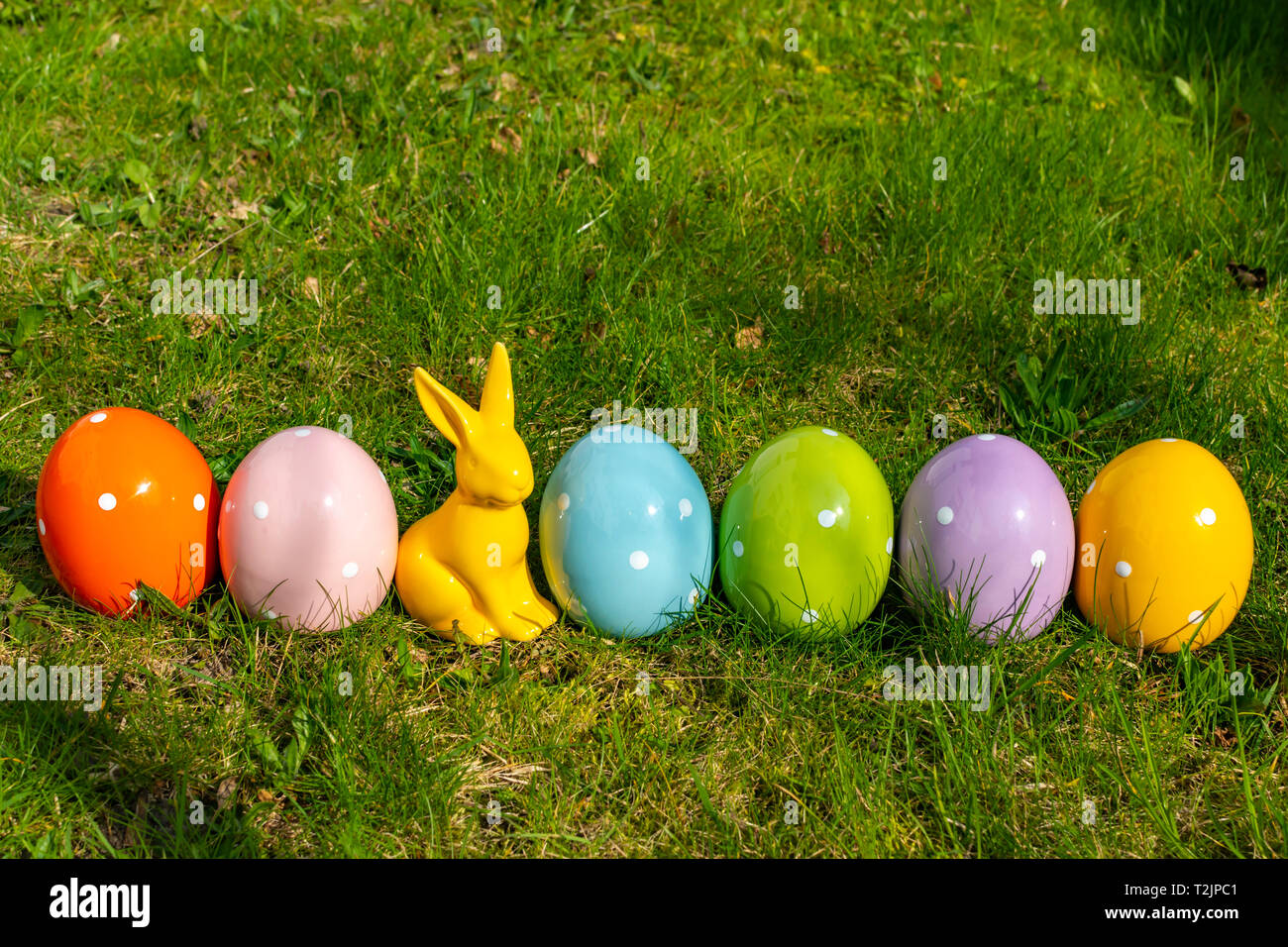 Colorful ceramic easter eggs and an Easter bunny in a line on a meadow. Stock Photo