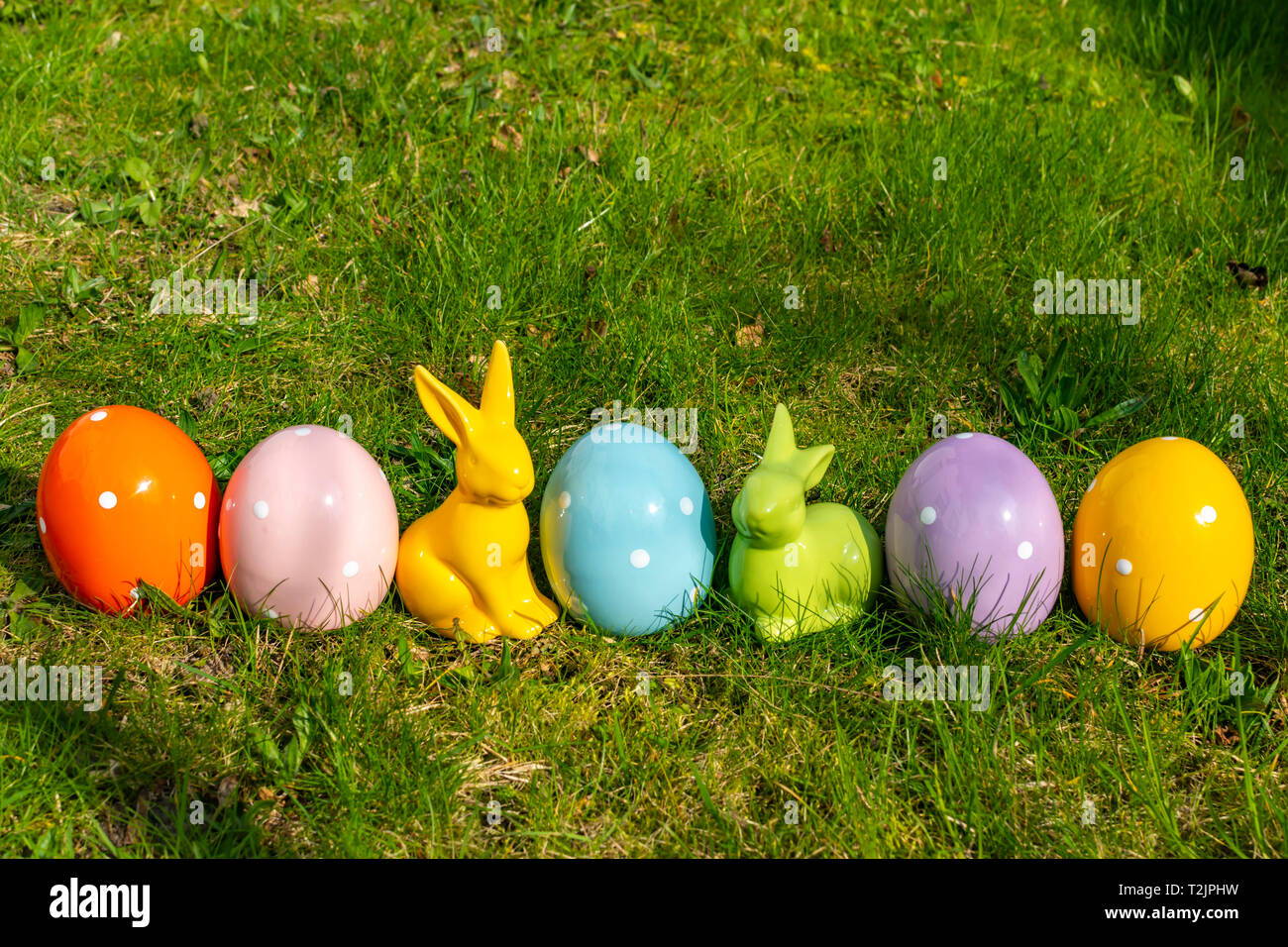 Colorful ceramic easter eggs and Easter bunnies in a line on a meadow. Stock Photo