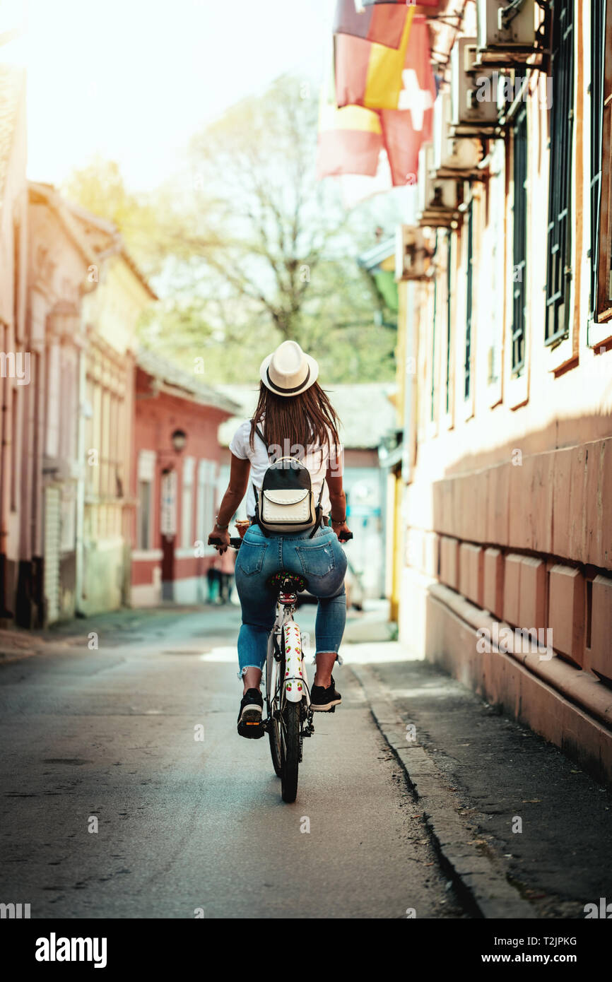 Happy woman is riding the bike along the city street, in summer sunny day, enjoying during outdoor activity. Stock Photo