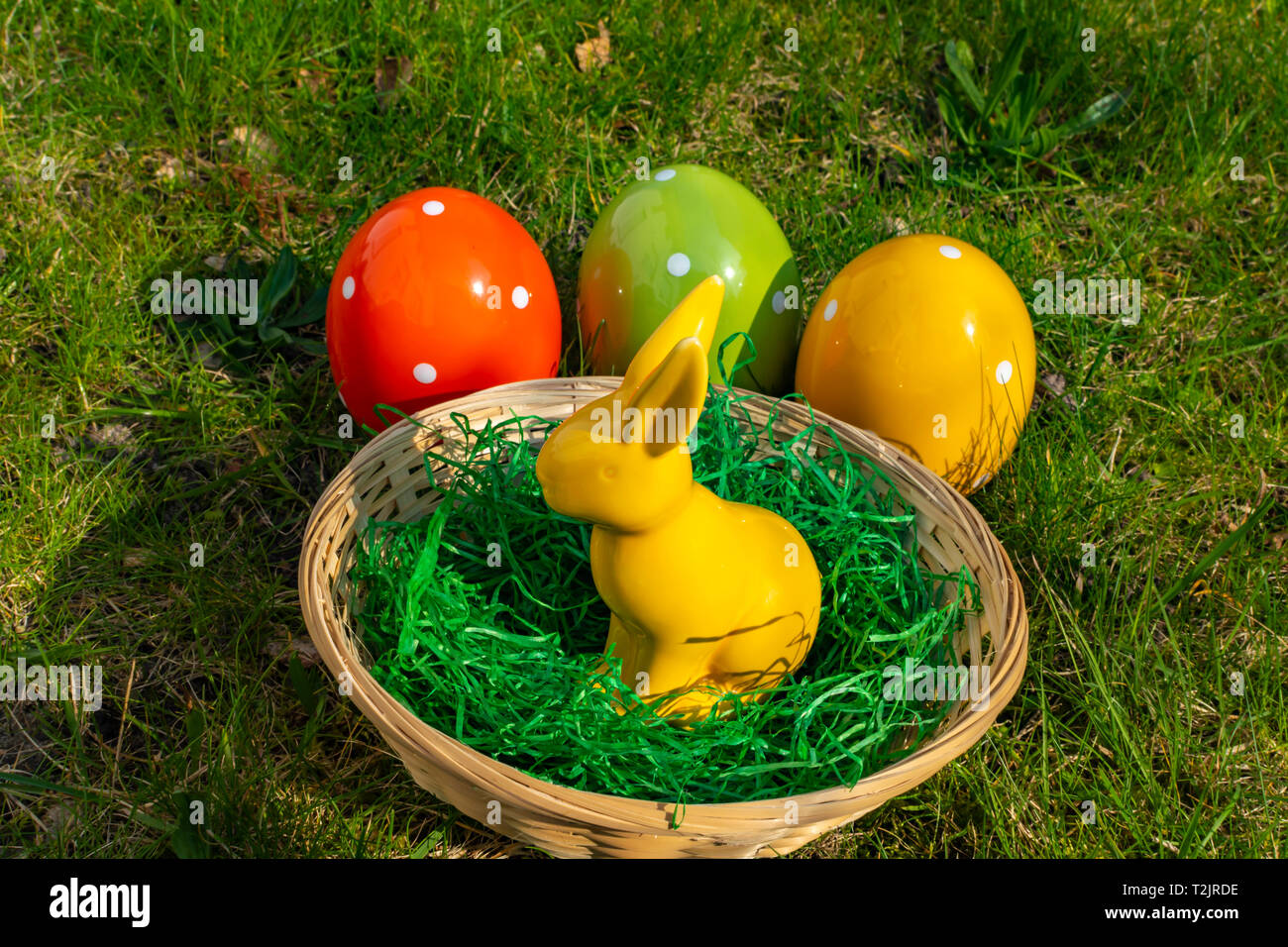 A yellow Easter bunny and colorful Easter eggs made of pottery with a basket on a meadow. Stock Photo
