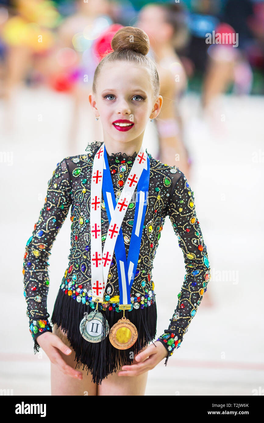 Little gymnast with her sports awards on the carpet in rhythmic