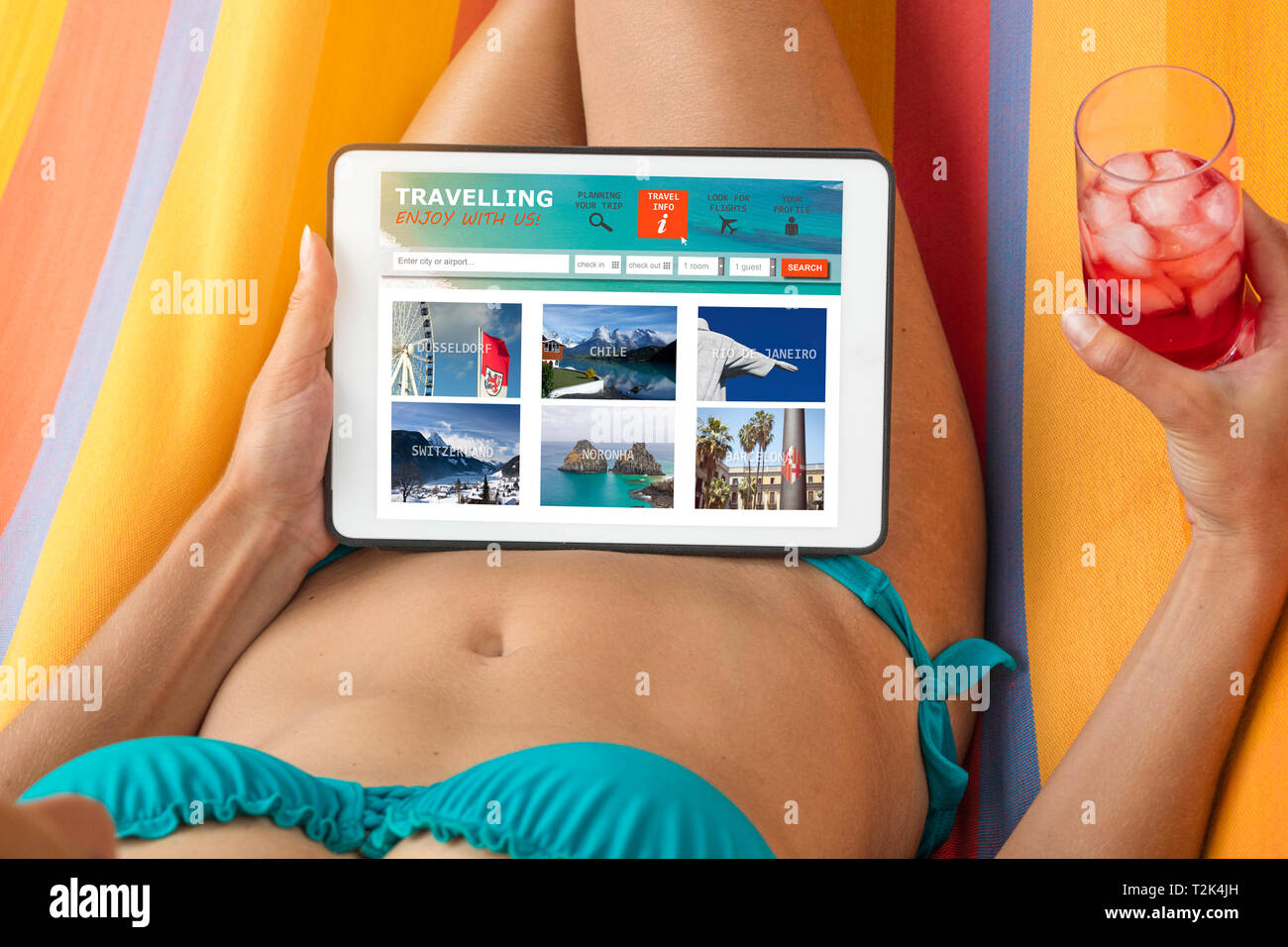 Young woman in a bikini visiting a travel website with tablet device, lying on a hammock and having a drink. Stock Photo