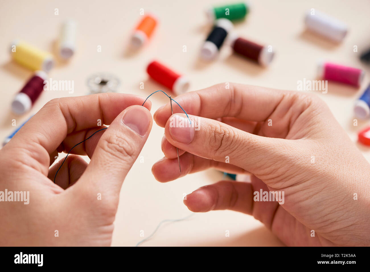 people, needlework, sewing and tailoring concept - tailor woman with thread in needle stitching fabric. Hands sewing with a needle and thread. Fingers Stock Photo