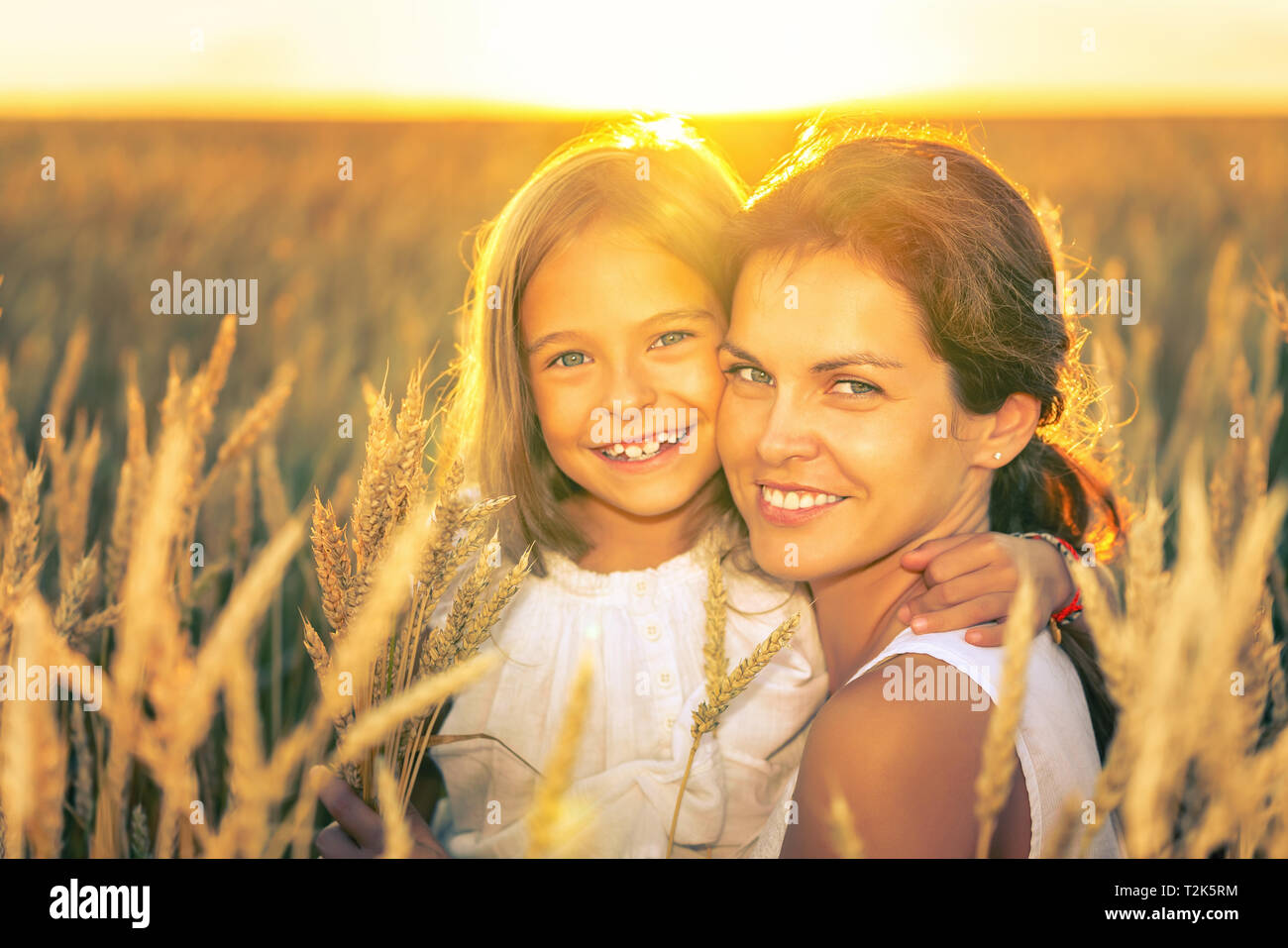 Young woman and her daughter on golden wheat field at sunny summer evening. Stock Photo