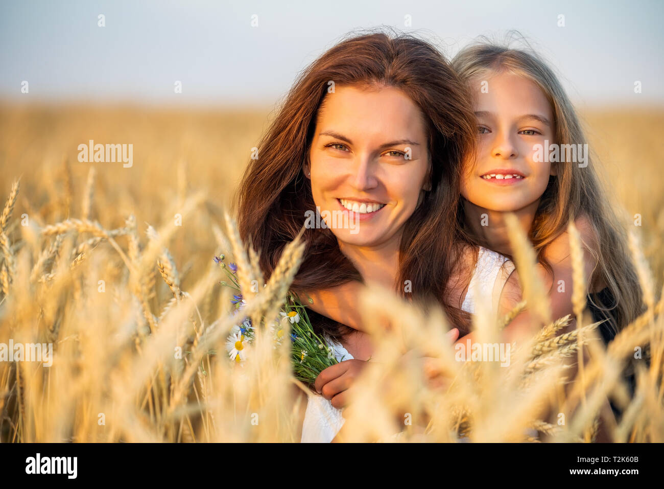 Young mother and her daughter on golden wheat field at summer evening. Stock Photo