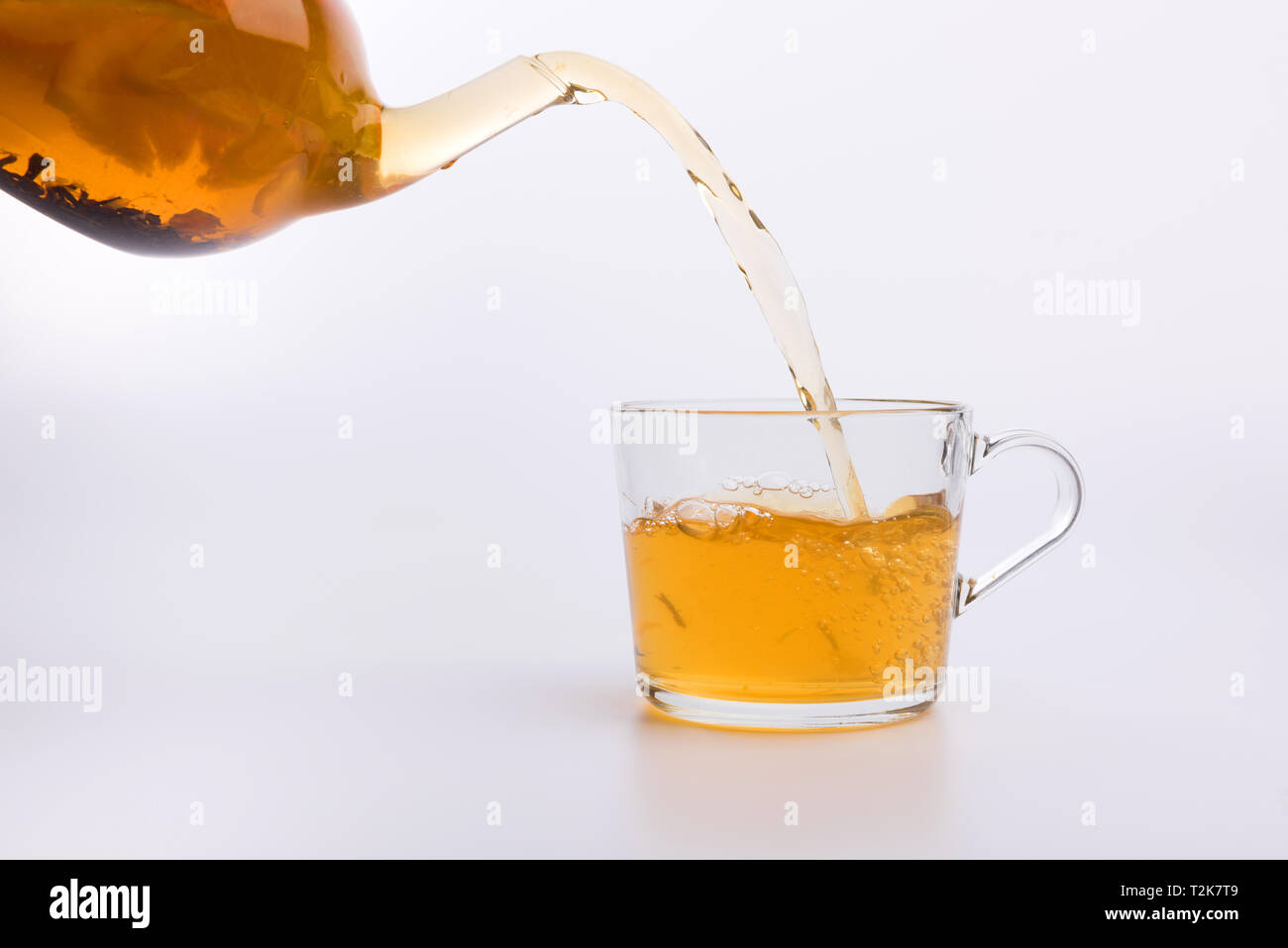 Glass teapot pouring green tea into cup isolated on white background