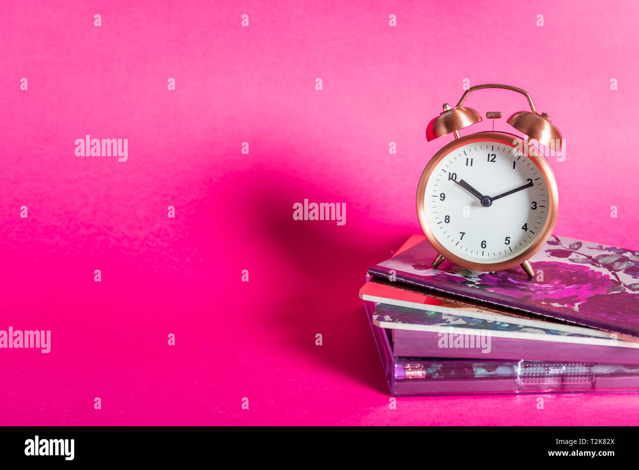 Different Notebooks And Alarm Clock On Bright Pink Background