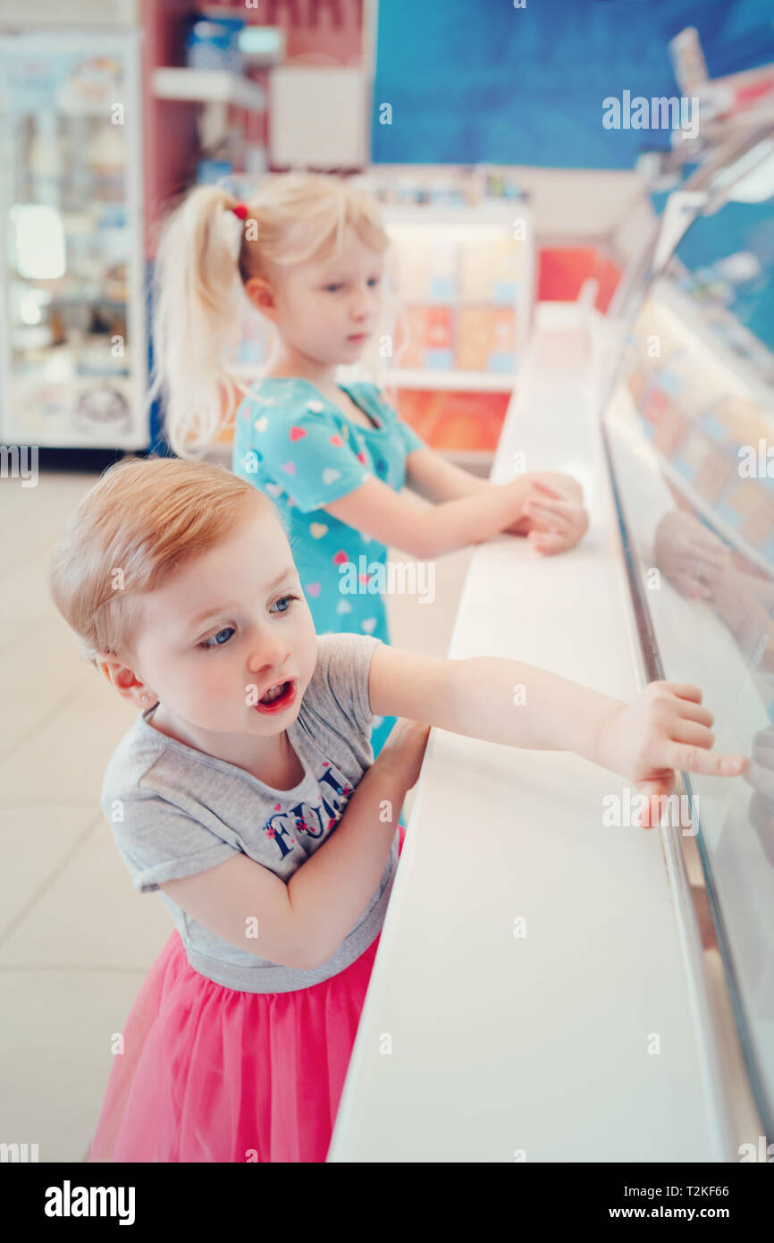 Two Caucasian girls children sisters friends looking at ice cream shop window and choosing tasty yummy summer food. Happy childhood lifestyle. Hard ch Stock Photo