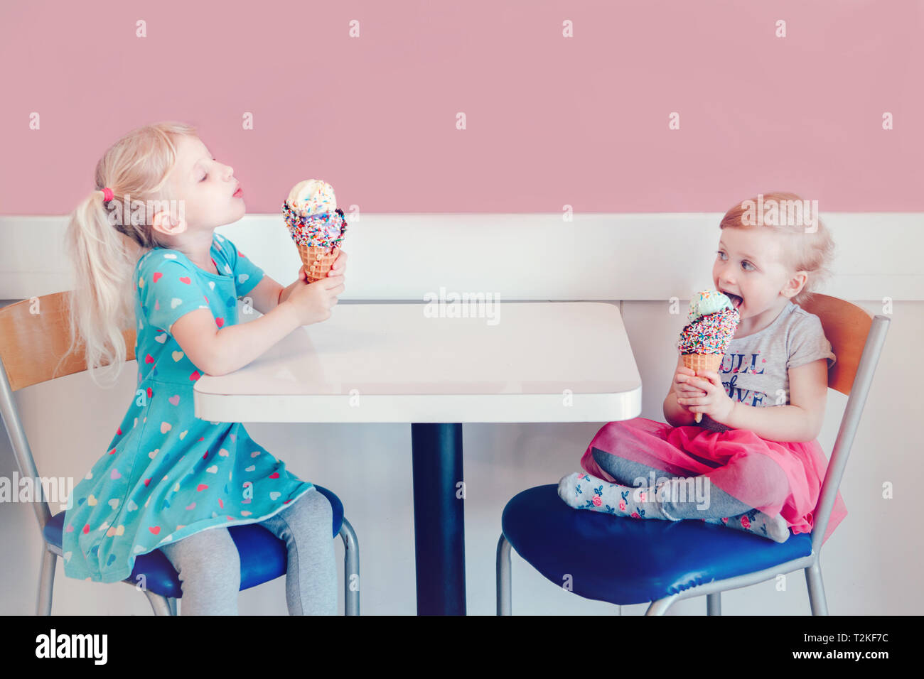 Lifestyle portrait of two happy Caucasian cute adorable funny children girls sitting together bragging boasting their ice-cream. Love envy jealous sis Stock Photo