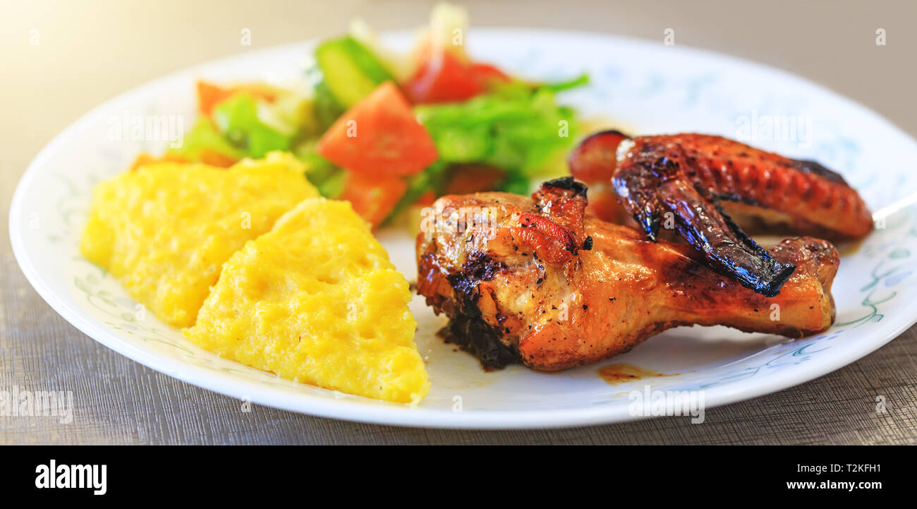 Baked chicken legs, Polenta or Mamaliga and salad in fancy plate. Traditional food and culinary culture specific for Balkan countries like Romania, Mo Stock Photo