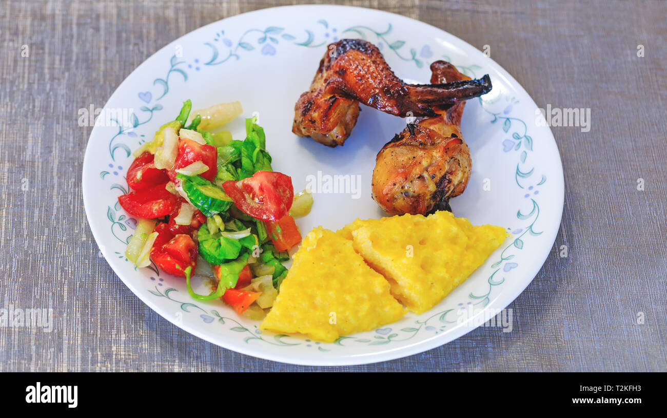 Mamaliga or polenta, baked chicken legs and salad in fancy plate. Traditional food and culinary culture specific for Balkan countries like Romania, Mo Stock Photo