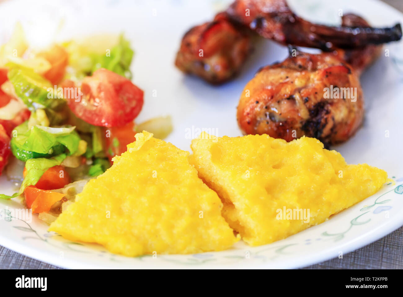 Polenta or Mamaliga, baked chicken legs and salad in fancy plate. Traditional food and culinary culture specific for Balkan countries like Romania, Mo Stock Photo
