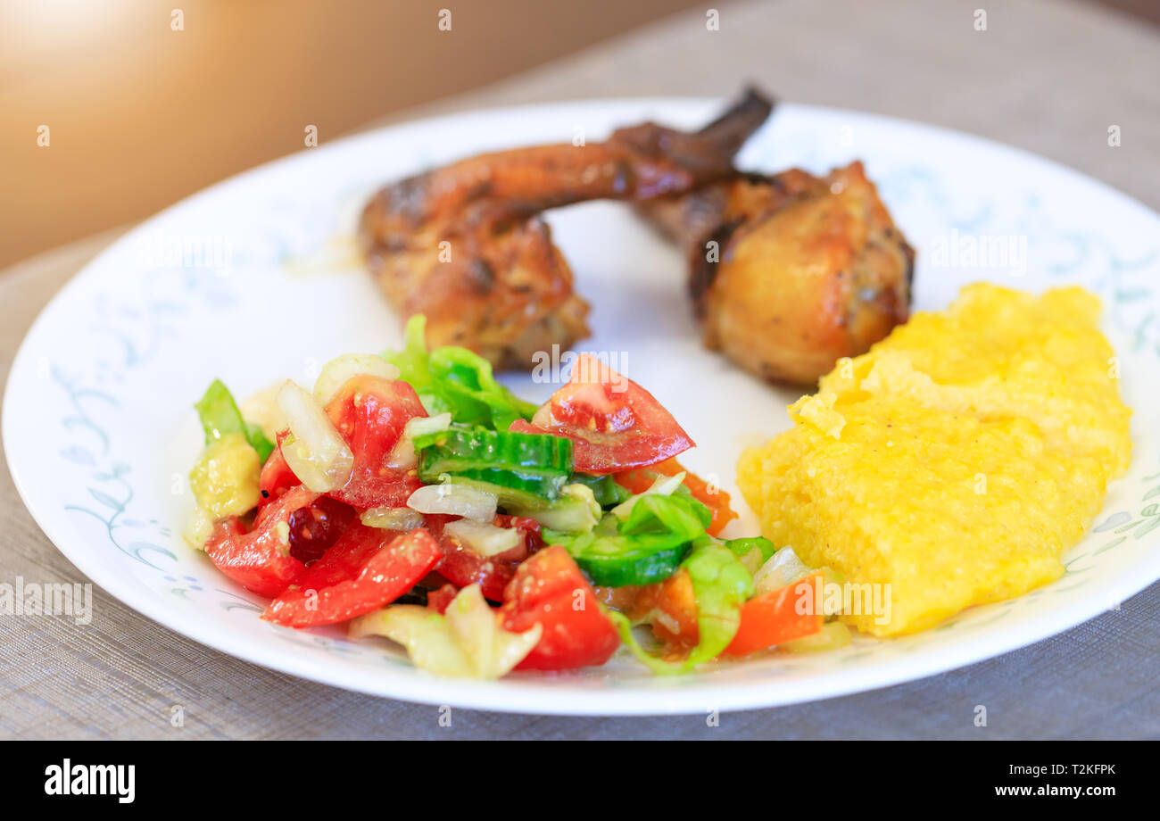 Salad, mamaliga or polenta, baked chicken legs in fancy plate. Traditional food and culinary culture specific for Balkan countries like Romania, Moldo Stock Photo