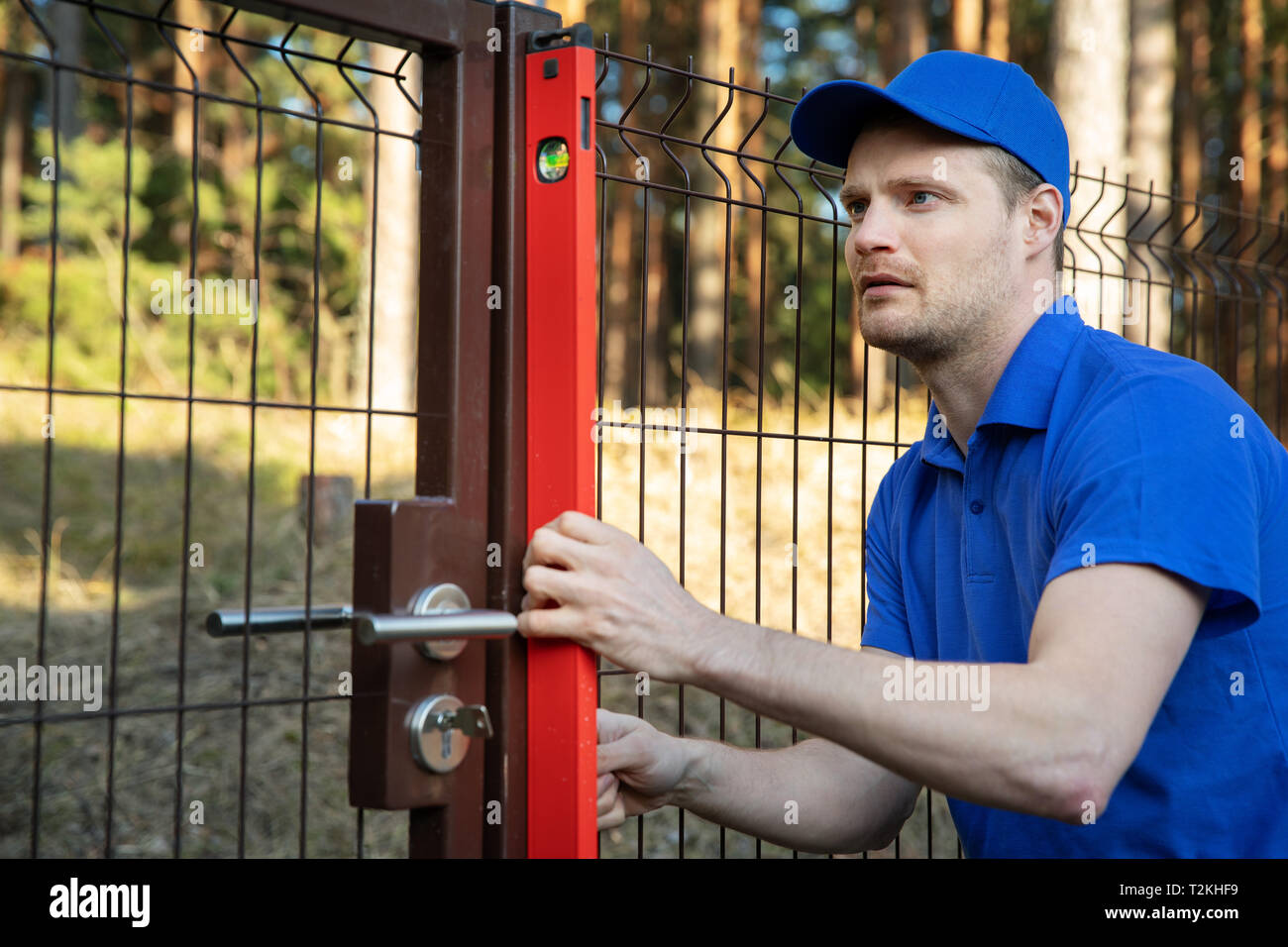 fence construction - worker check the level of metal post Stock Photo