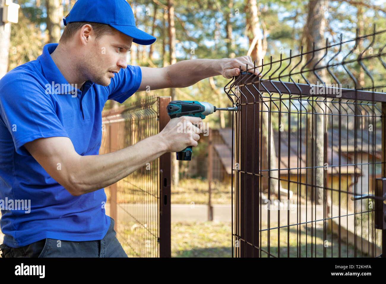 property territory fencing - man screws metal fence panel Stock Photo