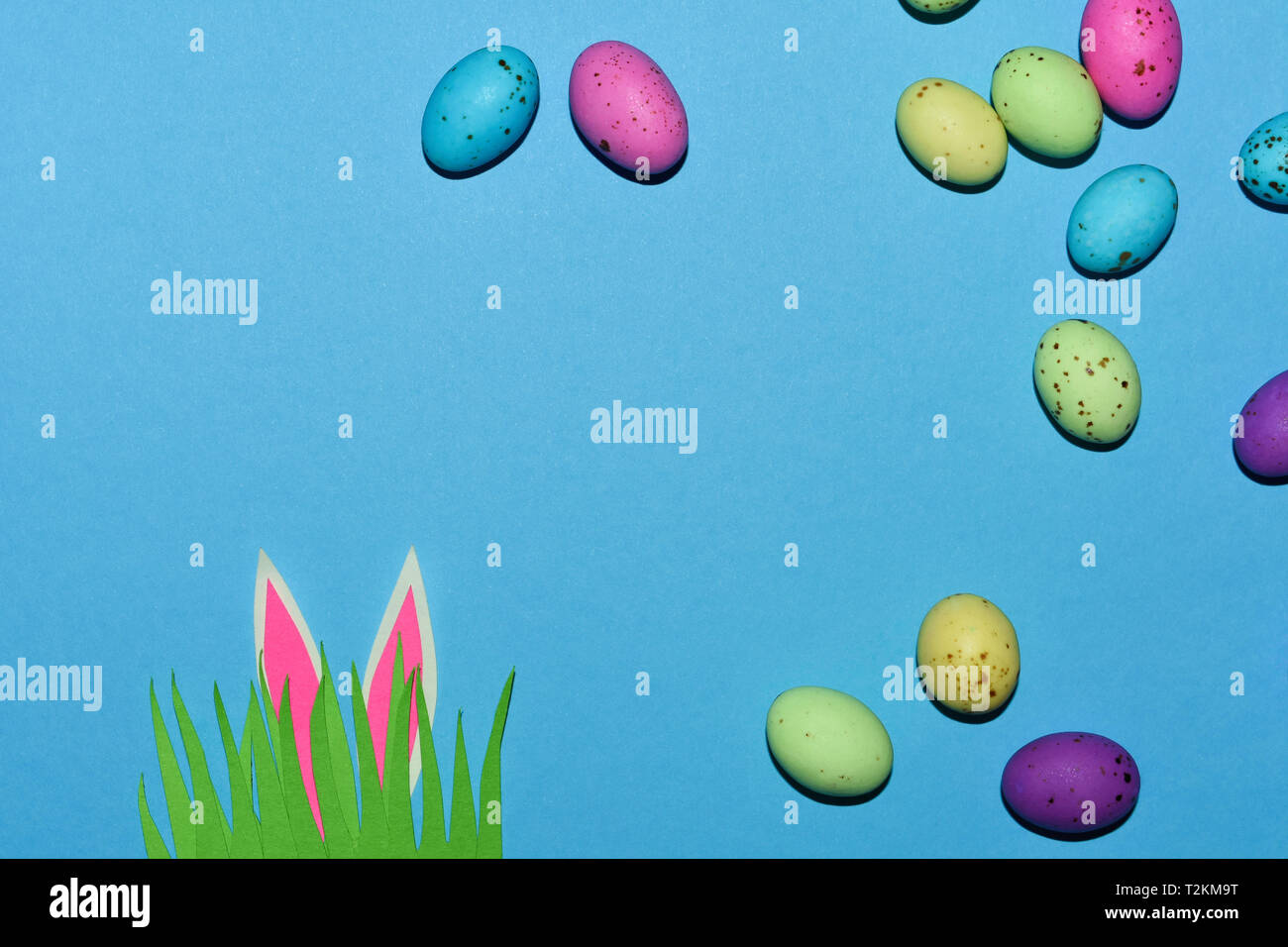 Candy Eggs On Blue With Grass Patch And Rabbit Ears Stock Photo