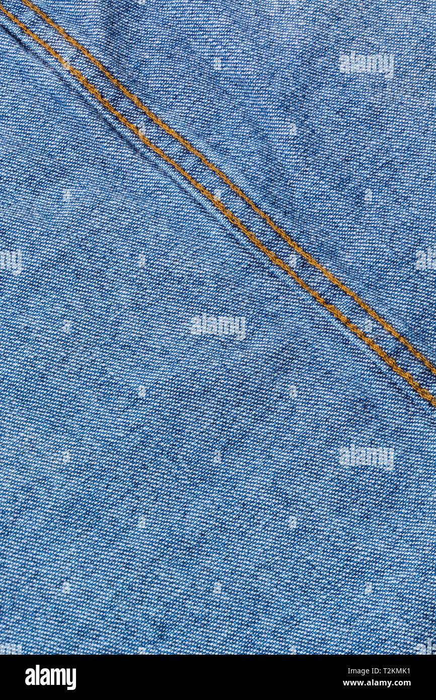 Close-up of blue denim fabric, showing warp and weft pattern thread pattern and orange stitching. Stitched line, line of stitches. Stock Photo