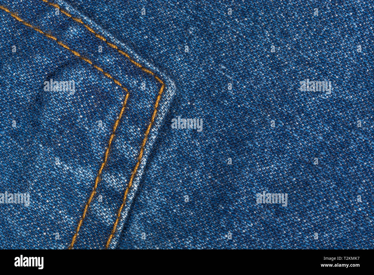 Close-up of blue denim fabric, showing warp and weft pattern thread pattern and orange stitching. Stitched line, line of stitches. Stock Photo