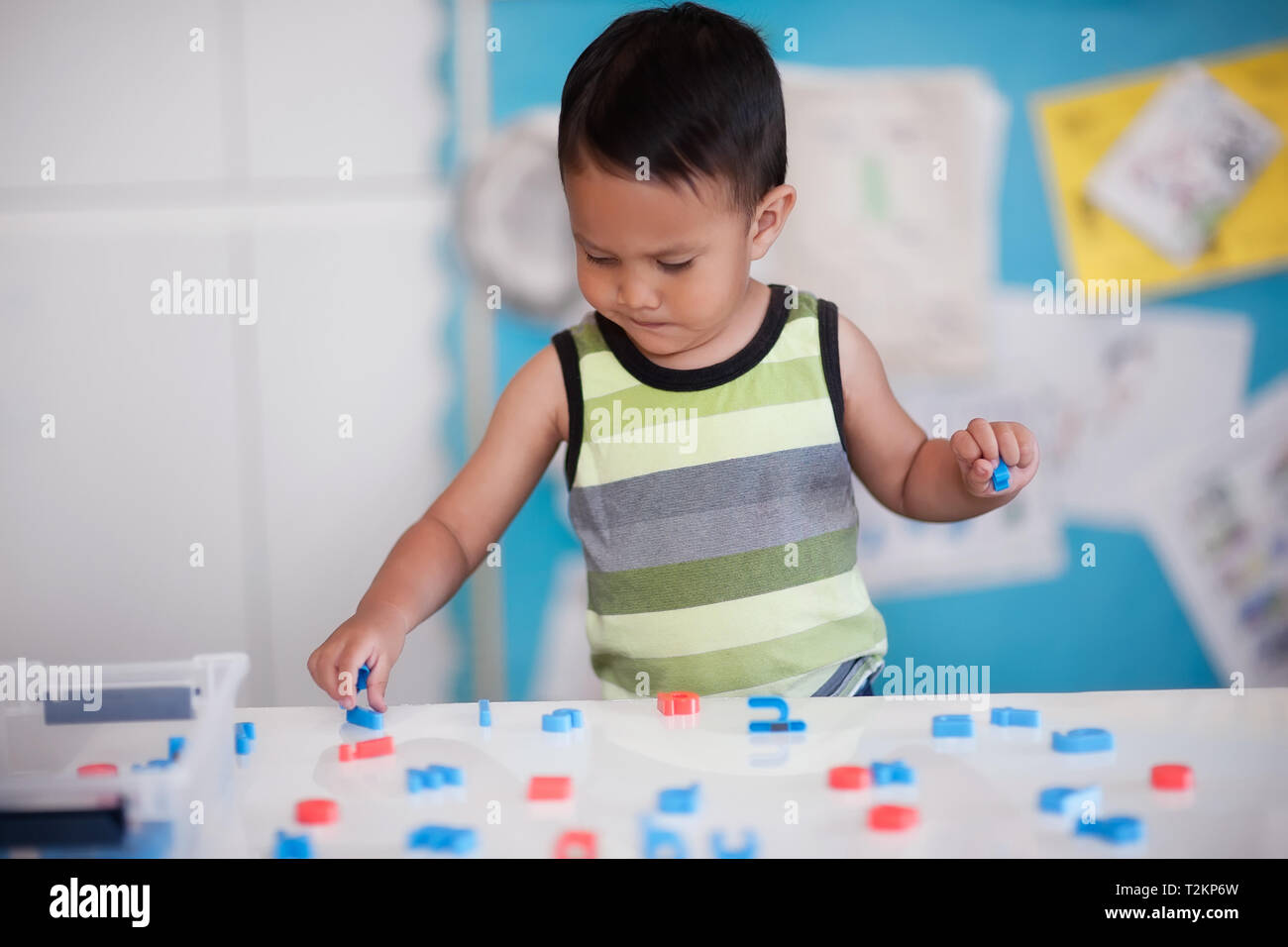 A smart young boy manipulating alphabet letters to form words in kindergarten room. Stock Photo