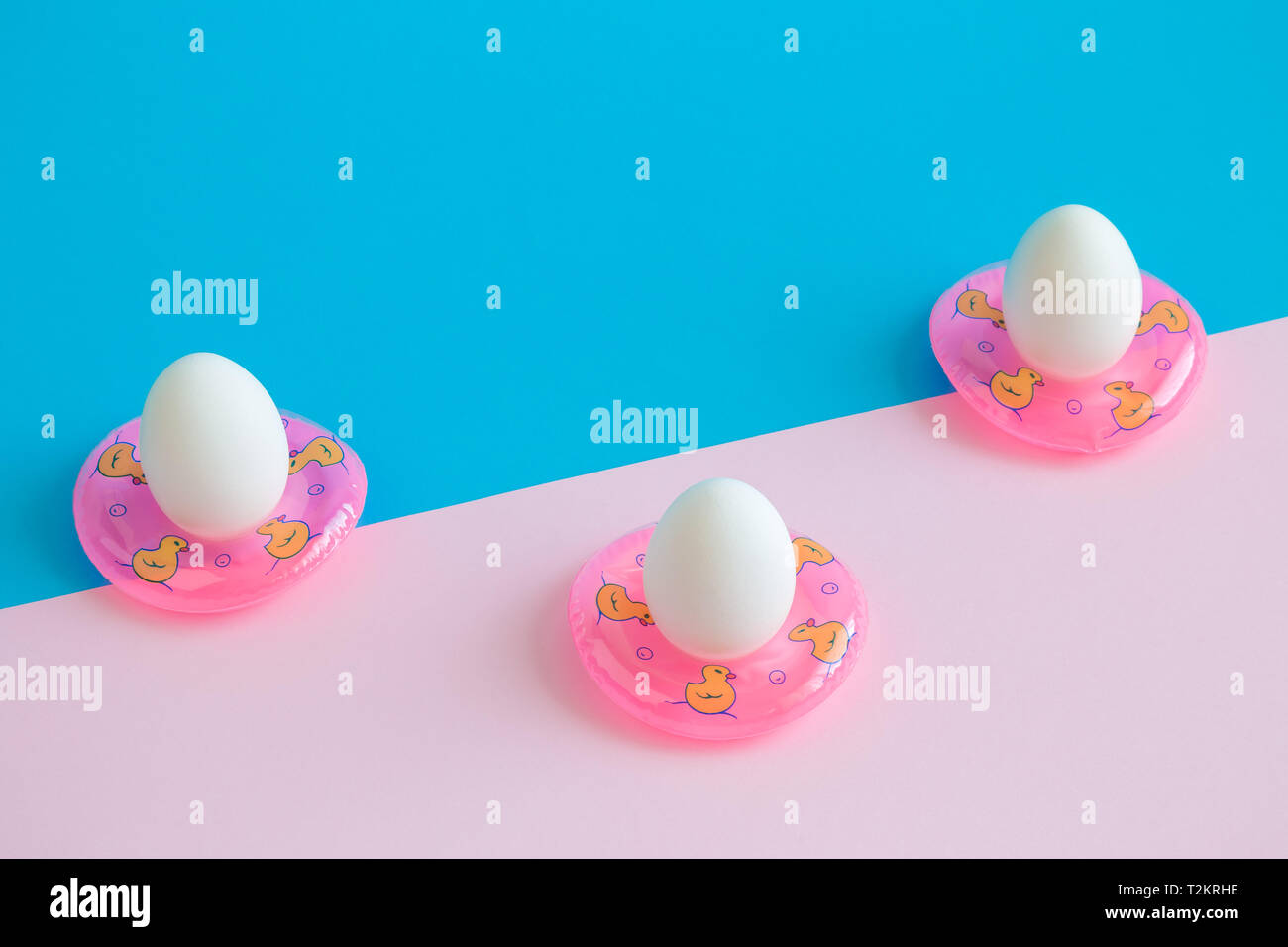 White eggs in swimming floats against pastel background minimal creative seasonal concept Stock