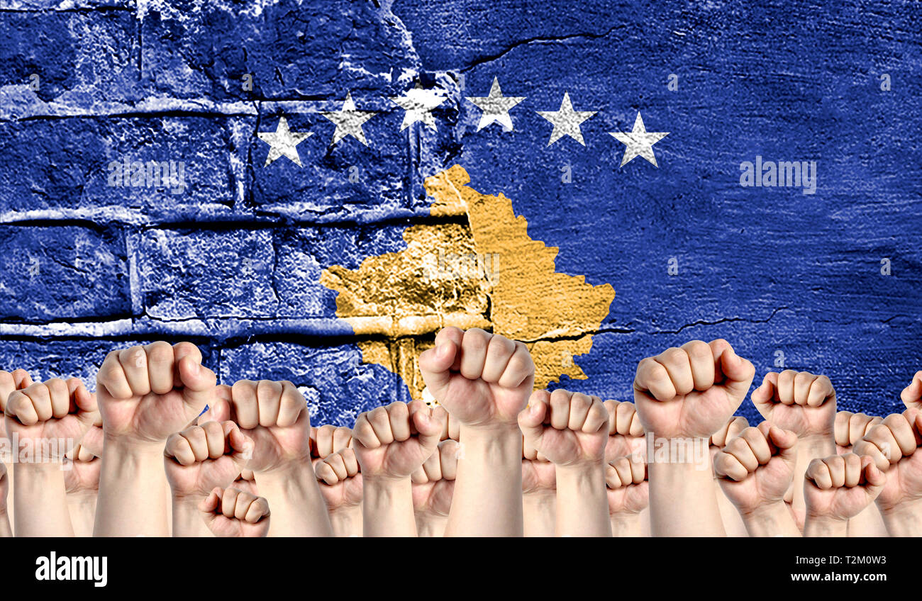 Male hands clenched in a fist raised up against the backdrop of a destroyed brick wall with a flag of Kosovo. The concept of the labor movement from t Stock Photo