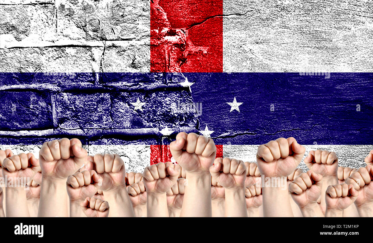 Male hands clenched in a fist raised up against the backdrop of a destroyed brick wall with a flag of Netherlands Antilles. The concept of the labor m Stock Photo