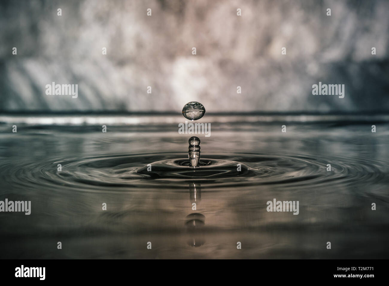 A drop of water impacts the surface forming circular waves Stock Photo