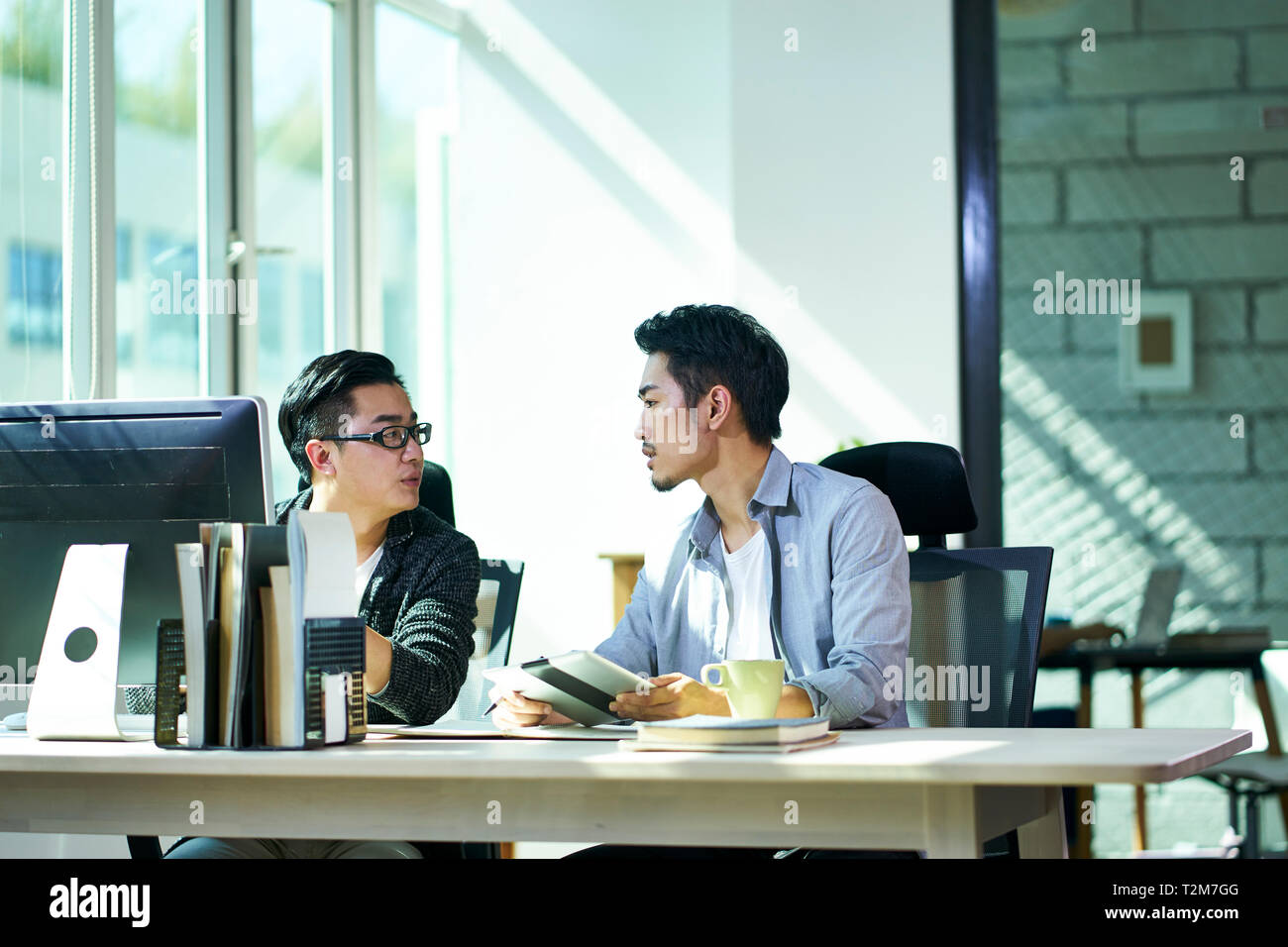 two young asian corporate executives working together discussing business plan in office. Stock Photo