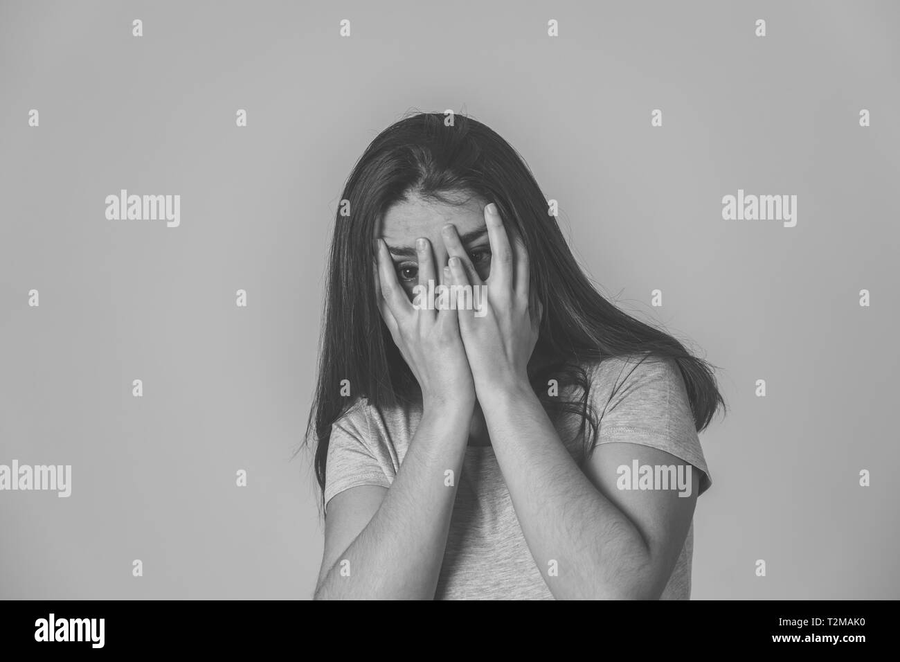 Black and white portrait of young woman feeling scared and shocked making fear, anxiety gestures. Looking terrified and covering herself. Copy space.  Stock Photo