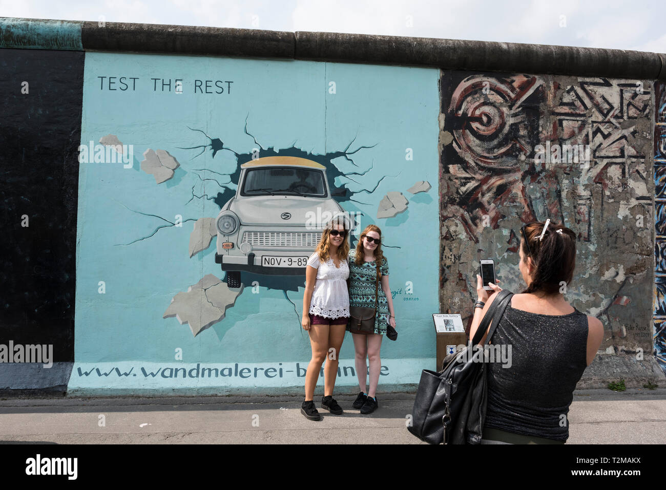 Berlin. Germany. Tourists pose for photos infront of Birgit Kinder's famous mural 'Test the Rest' on the Berlin Wall at the East Side Gallery. Stock Photo