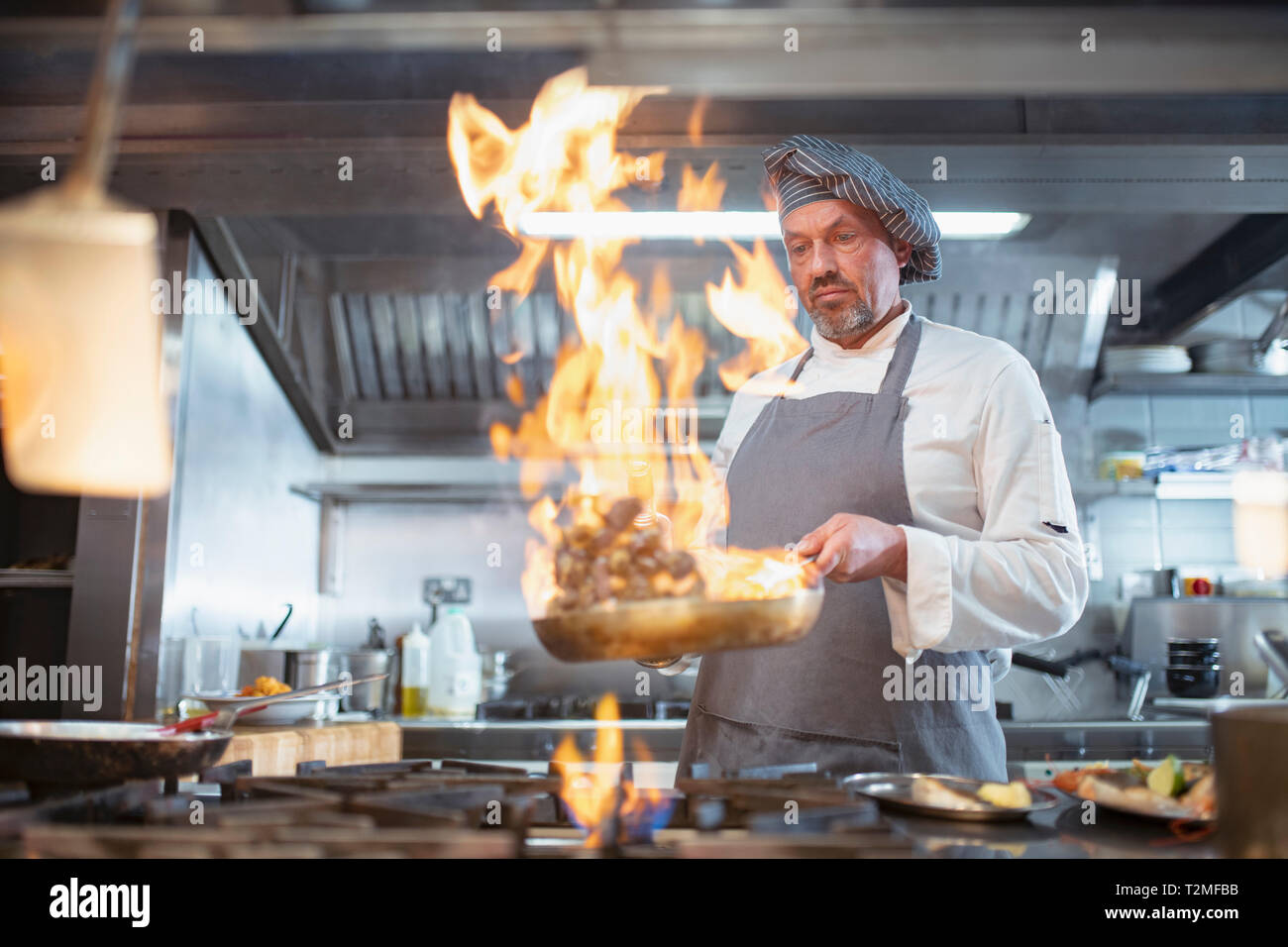 Chef cooking with brandy (flambe) and flames in Italian restaurant kitchen Stock Photo