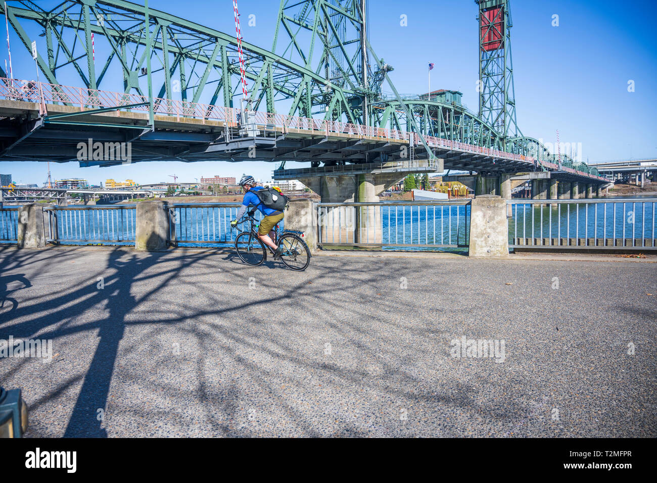 Cyclist pedals a bicycle and rides along the Portland waterfront with bridge, preferring, like most Portland residents, an active healthy lifestyle an Stock Photo