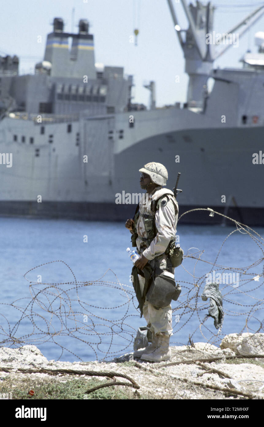30th October 1993 A black U.S. Army soldier of the 24th Infantry Division, 1st Battalion of the 64th Armored Regiment, stands at the water's edge in the new port in Mogadishu, Somalia. In the background is the huge United States Marine Administration vehicle cargo ship, USNS Denebola. Stock Photo