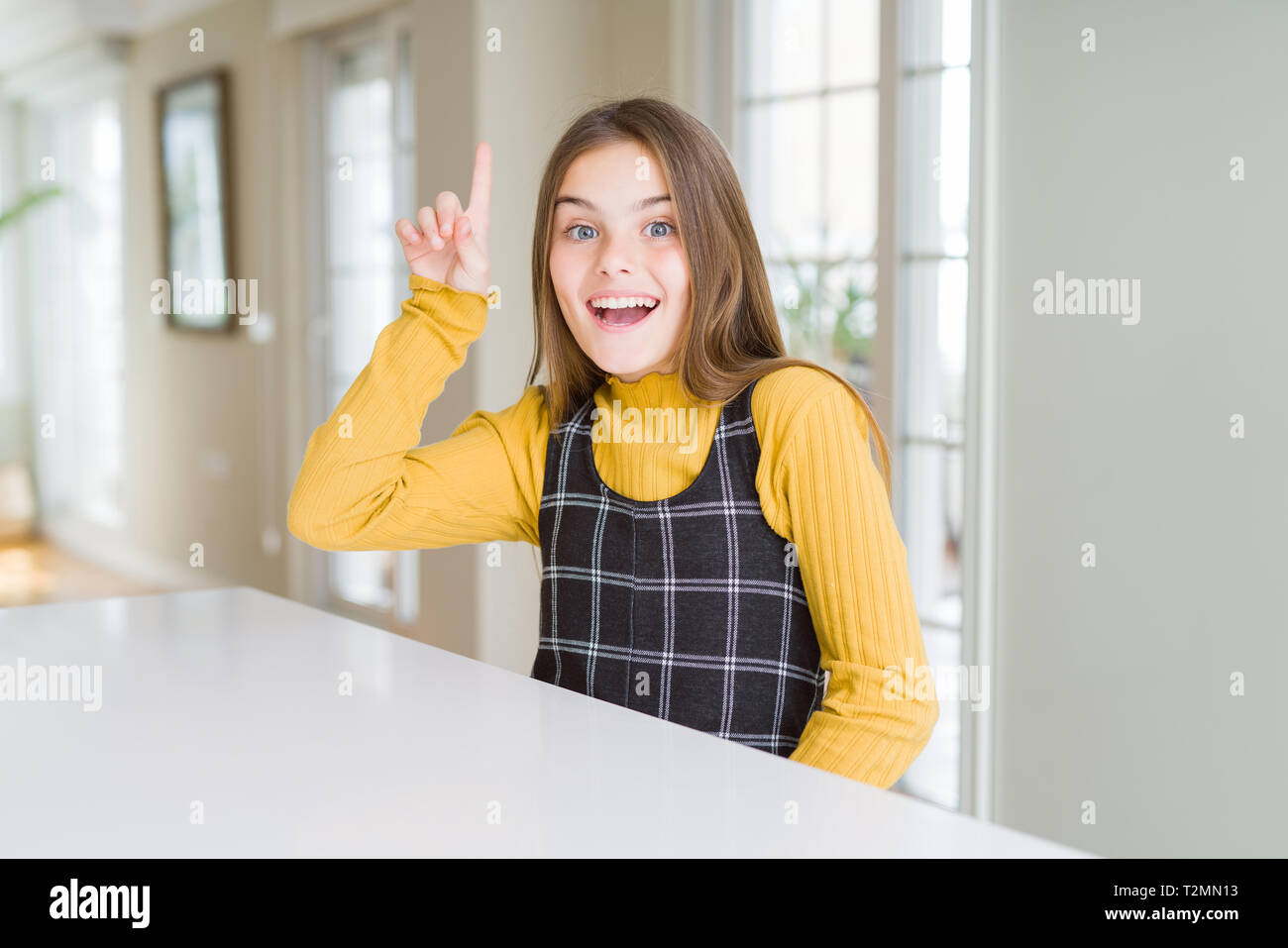 Beautiful young girl kid sitting on the table pointing finger up with ...