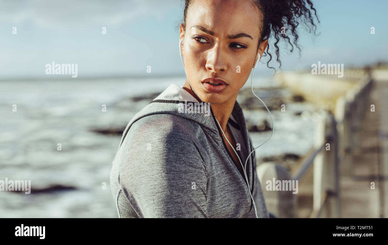 Sporty young woman standing on the promenade and looking away. Female runner resting after a run. Stock Photo