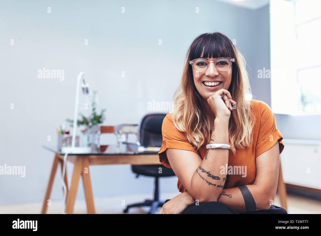 Close up of a smiling woman entrepreneur sitting in her cabin at office. Smiling businesswoman sitting in office resting her chin on hand. Stock Photo