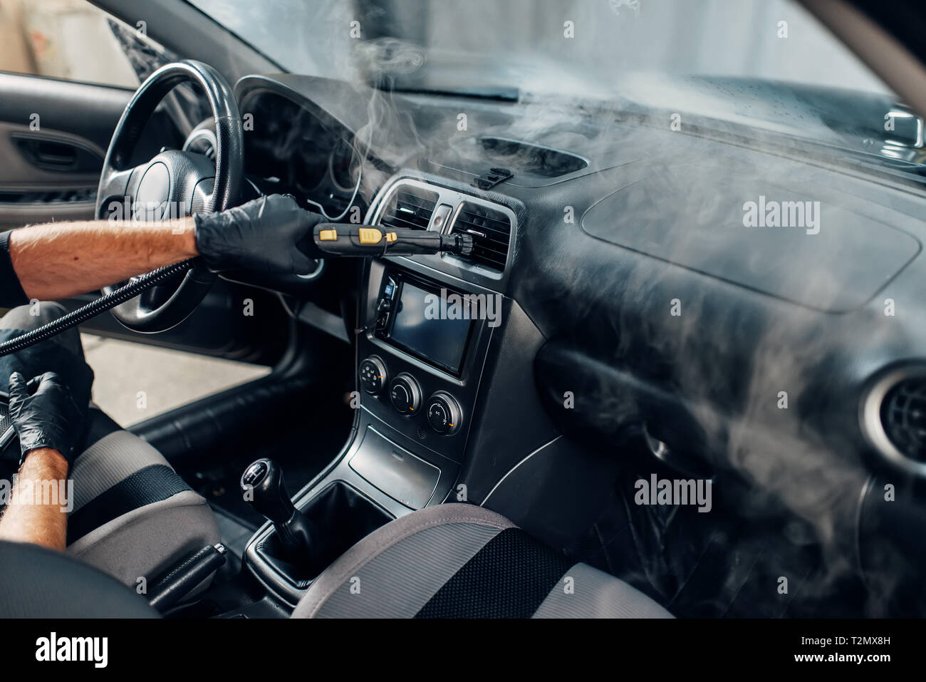 carwash service worker in gloves cleans salon with steam cleaner professional dry cleaning of car interior T2MX8H