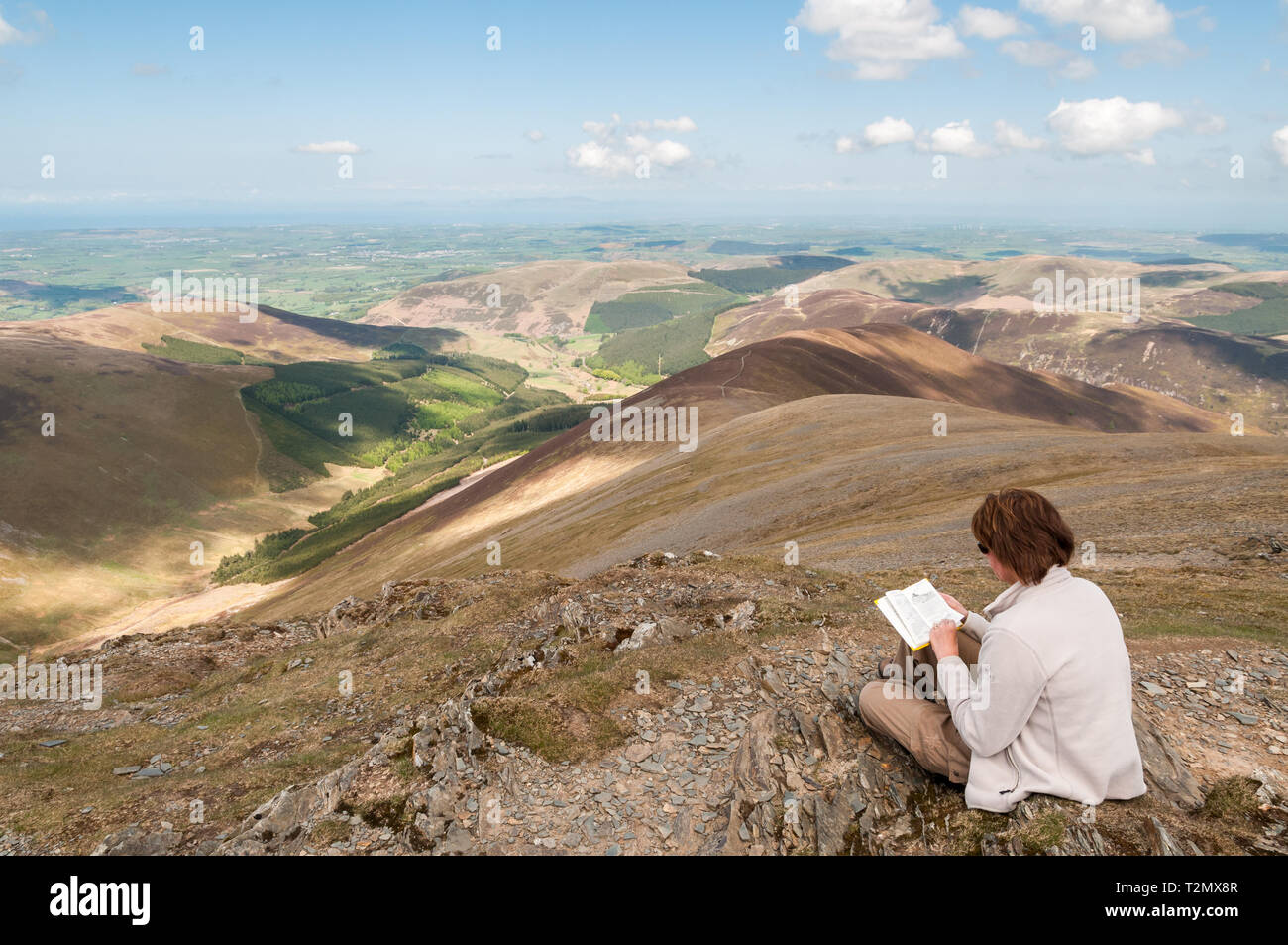 A woman is sitting near the summit of Grisedale Pike in the English Lake District.  Grisedale Pike is one of the Wainwright Fells in the National Park Stock Photo