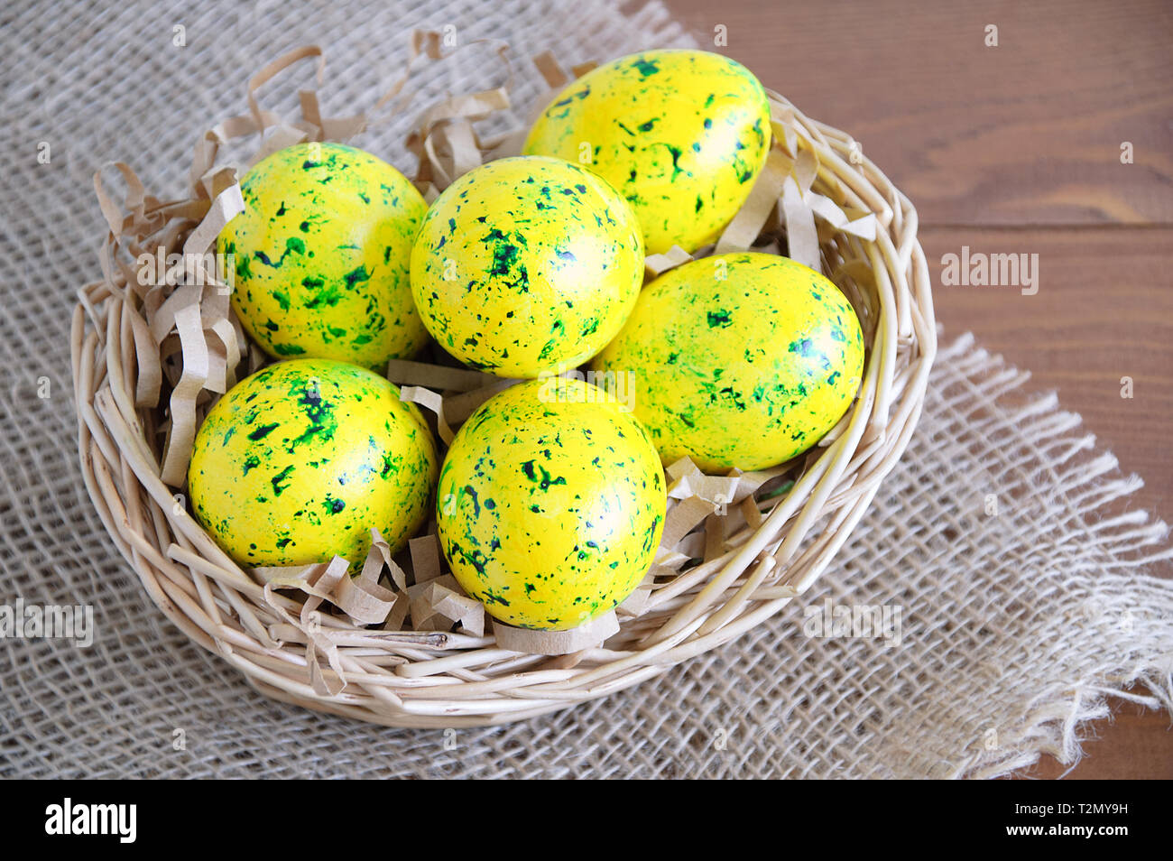 Yellow Easter eggs in a basket. On linen fabric brown. Wooden brown background. Stock Photo
