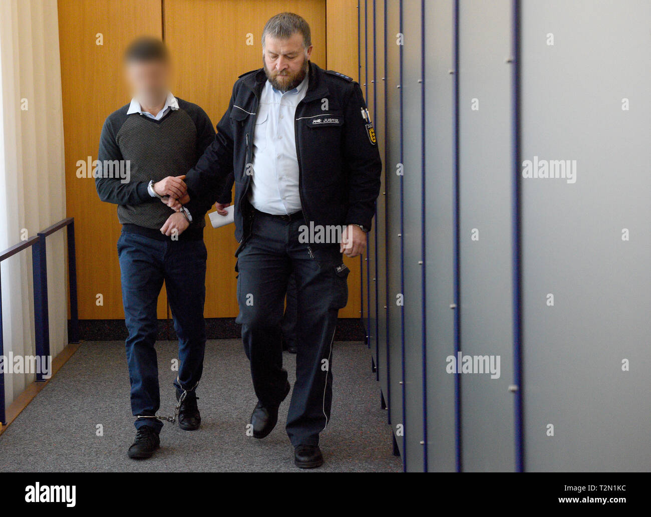 02 April 2019, Baden-Wuerttemberg, Ulm: In the district court, a judicial watchman (r) presents the accused, who is tied to his hands and feet. About two years after the murder of a young Albanian in Germany, the Ulm Regional Court announced the verdict. The accused, who is also of Albanian origin, is said to have played a central role in the murder of the victim, according to the public prosecutor's office. The motive was an archaic "blood revenge" in the course of a feud between hostile families in Albania. The court sentenced the accused to life imprisonment for murder. Photo: Stefan Puchne Stock Photo