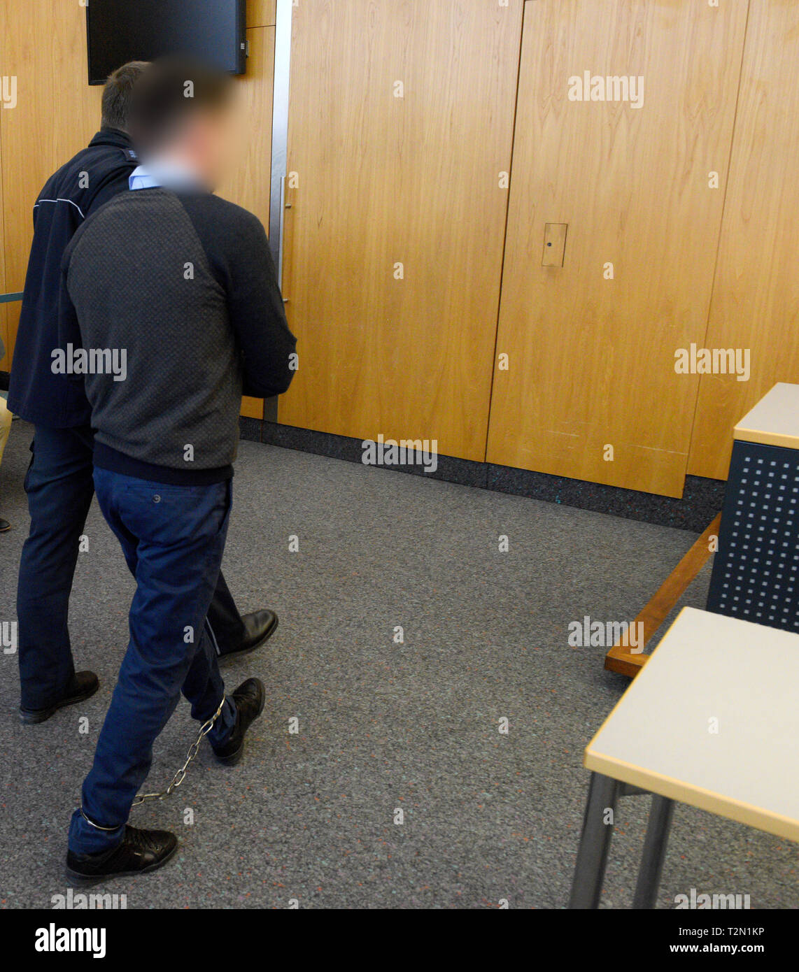 02 April 2019, Baden-Wuerttemberg, Ulm: In the district court, a judicial watchman (l) presents the accused, who is tied to his hands and feet. About two years after the murder of a young Albanian in Germany, the Ulm Regional Court announced the verdict. The accused, who is also of Albanian origin, is said to have played a central role in the murder of the victim, according to the public prosecutor's office. The motive was an archaic 'blood revenge' in the course of a feud between hostile families in Albania. The court sentenced the accused to life imprisonment for murder. Photo: Stefan Puchne Stock Photo
