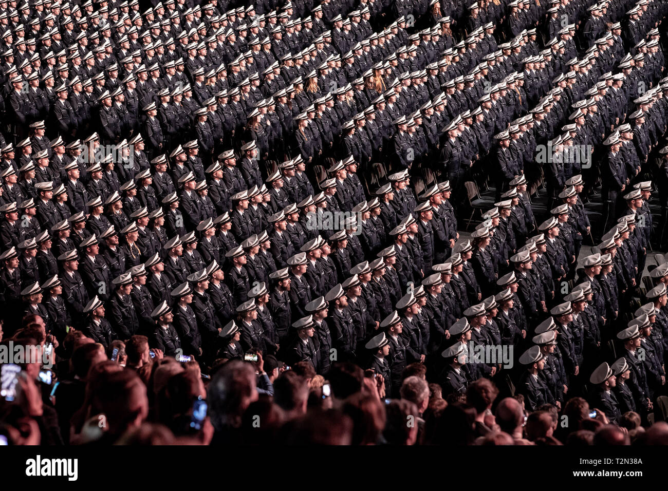Cologne, Germany. 03rd Apr, 2019. 03 April 2019, North Rhine-Westphalia, Köln: Commissioner candidates stand in front of their chairs during the swearing-in ceremony and are filmed by relatives. 2300 Commissioner candidates of the 2018 police recruitment year have taken their oath of allegiance. Photo: Marcel Kusch/dpa Credit: dpa picture alliance/Alamy Live News Stock Photo