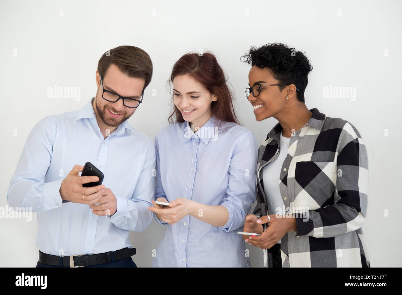 Group of people standing together opposite white wall looking on  smartphone. Man showing to colleagues girls funny video or interesting  news. Social n Stock Photo - Alamy