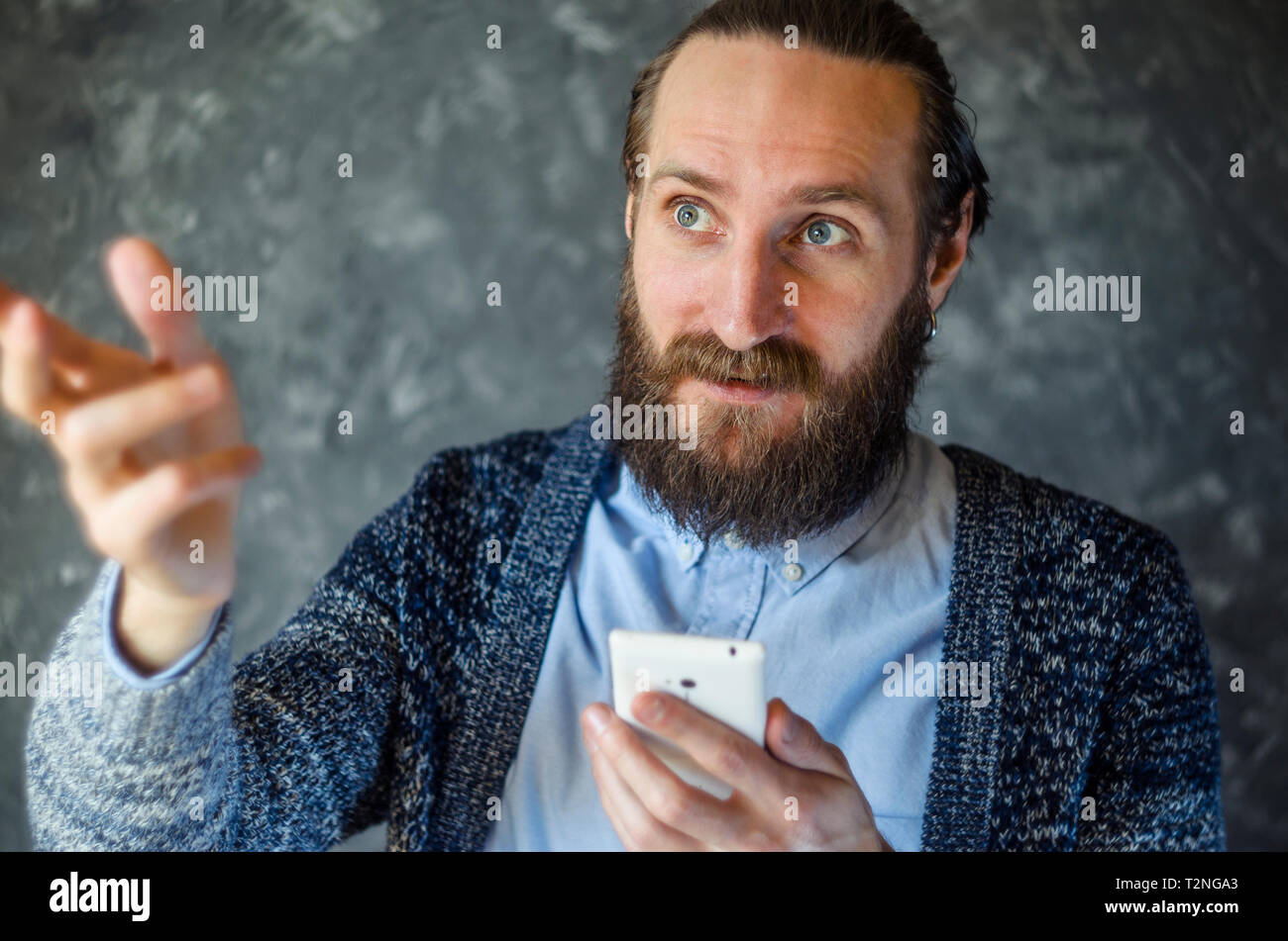 Bearded Man Have Business Meeting Via Video Call and Gesticulates During Conversation Against Gray Wall in a Office Stock Photo