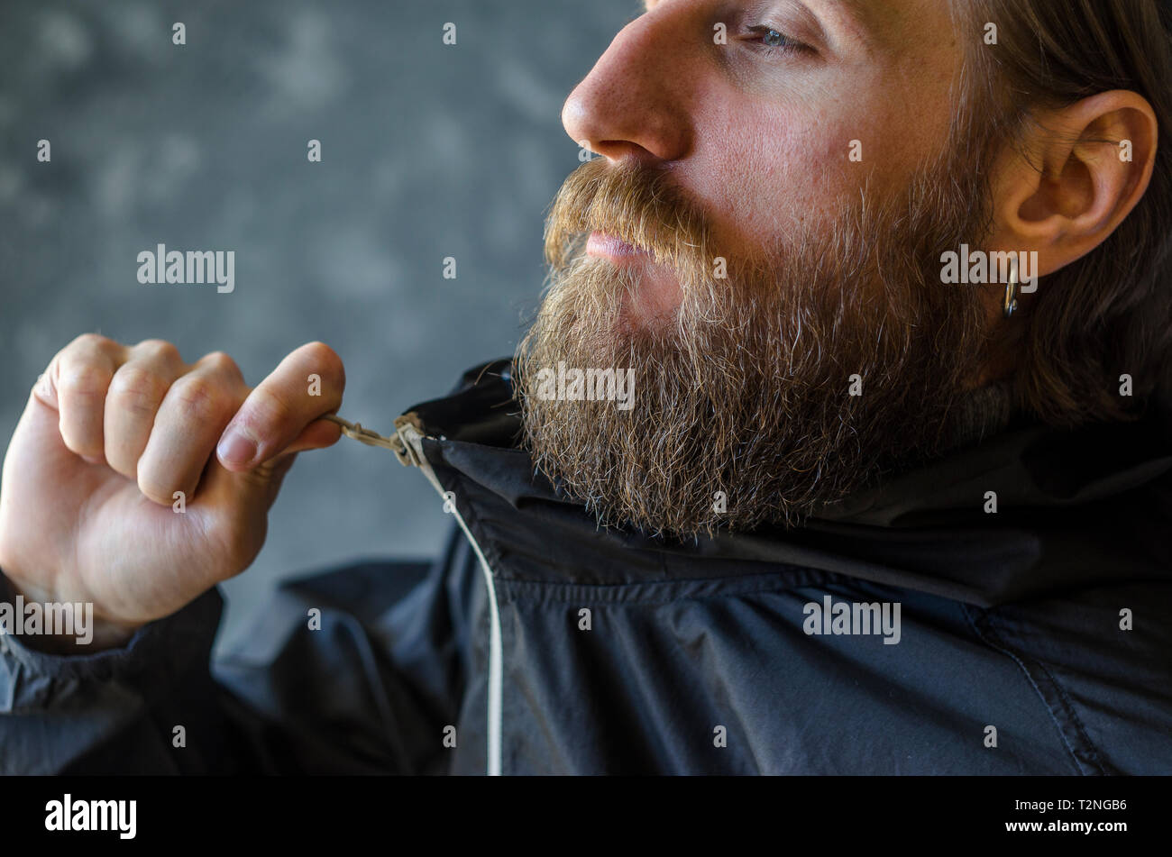 Man with a Beard Zip Up the Zipper in a Black Sports Jacket. Youth Type of Clothing Concept Stock Photo
