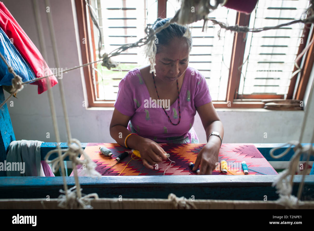 A Nepali woman embroidering silk and pashmina wool shawls by loom, at W.F. Nepal, an NGO employing marginalised women on a equal rights basis. Stock Photo
