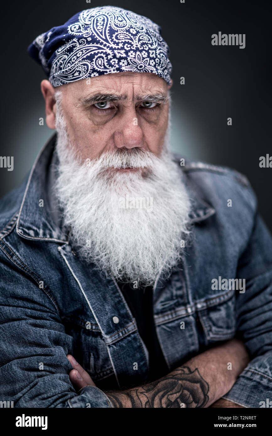 studio portrait of a senior hipster with tattooed arms, wearing a bandana and a long white beard Stock Photo