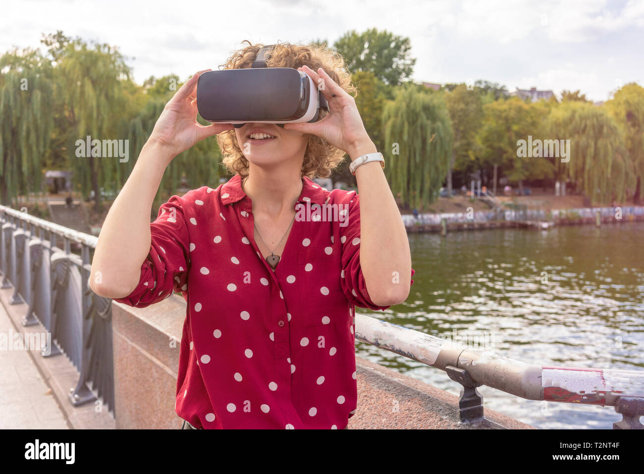 Young woman using VR headset on bridge, river in background, Berlin, Germany Stock Photo