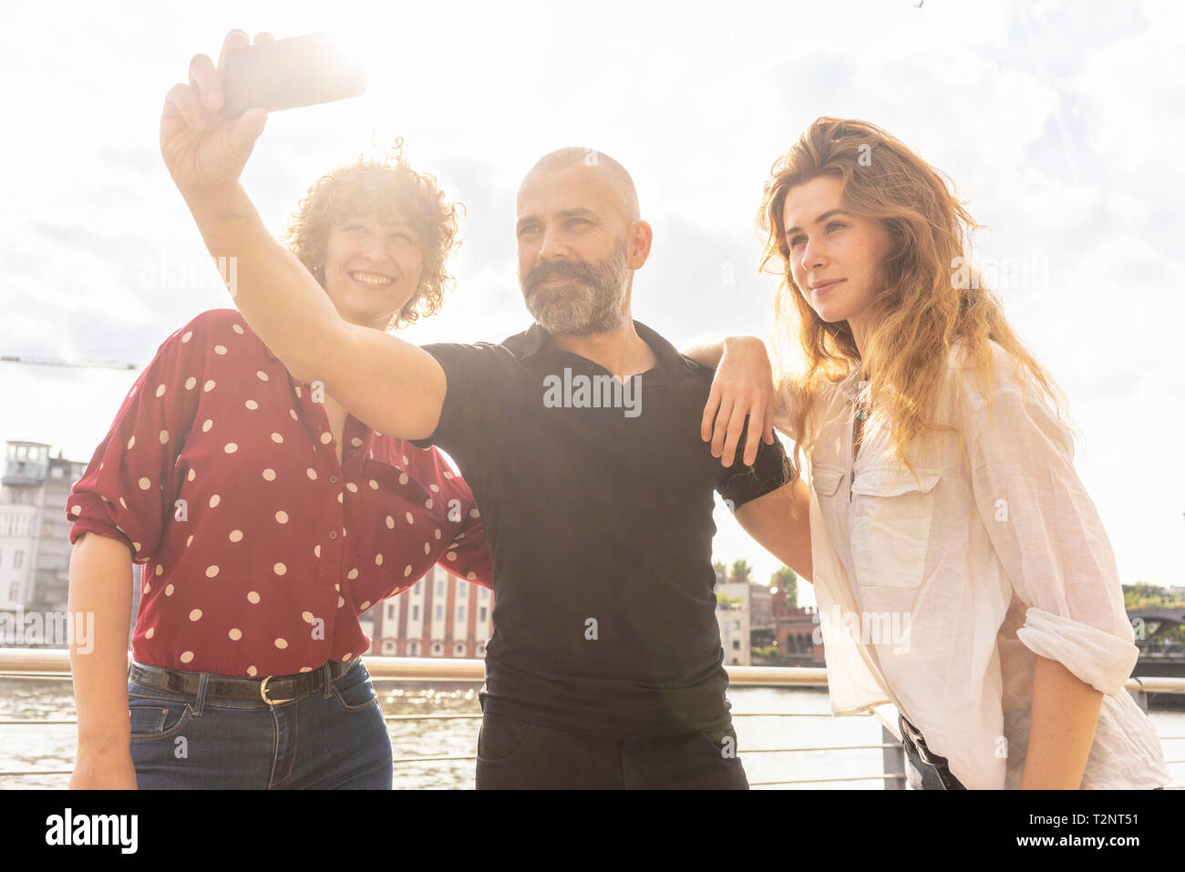 Man and female friends taking selfie with smartphone on bridge Stock Photo